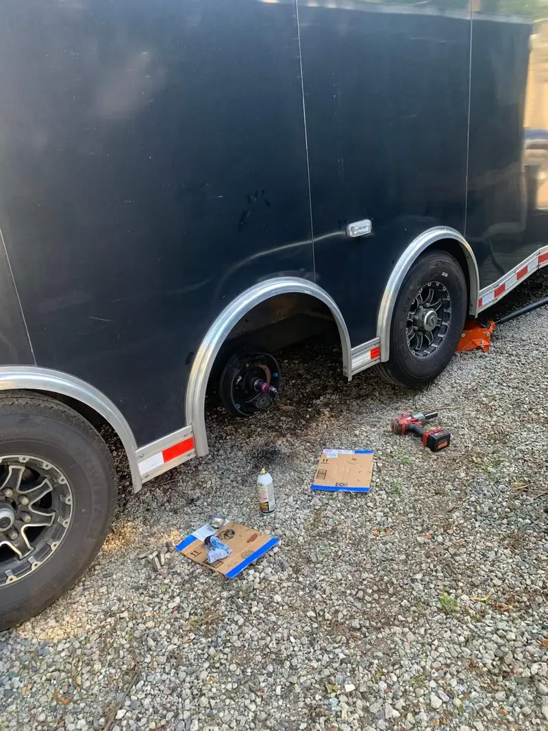Black enclosed car hauler with one wheel removed for hub and brake service on a gravel lot