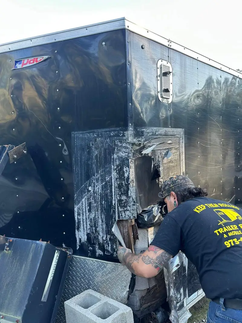 Keep Them Rolling technician repairing a damaged rear corner on a black enclosed trailer