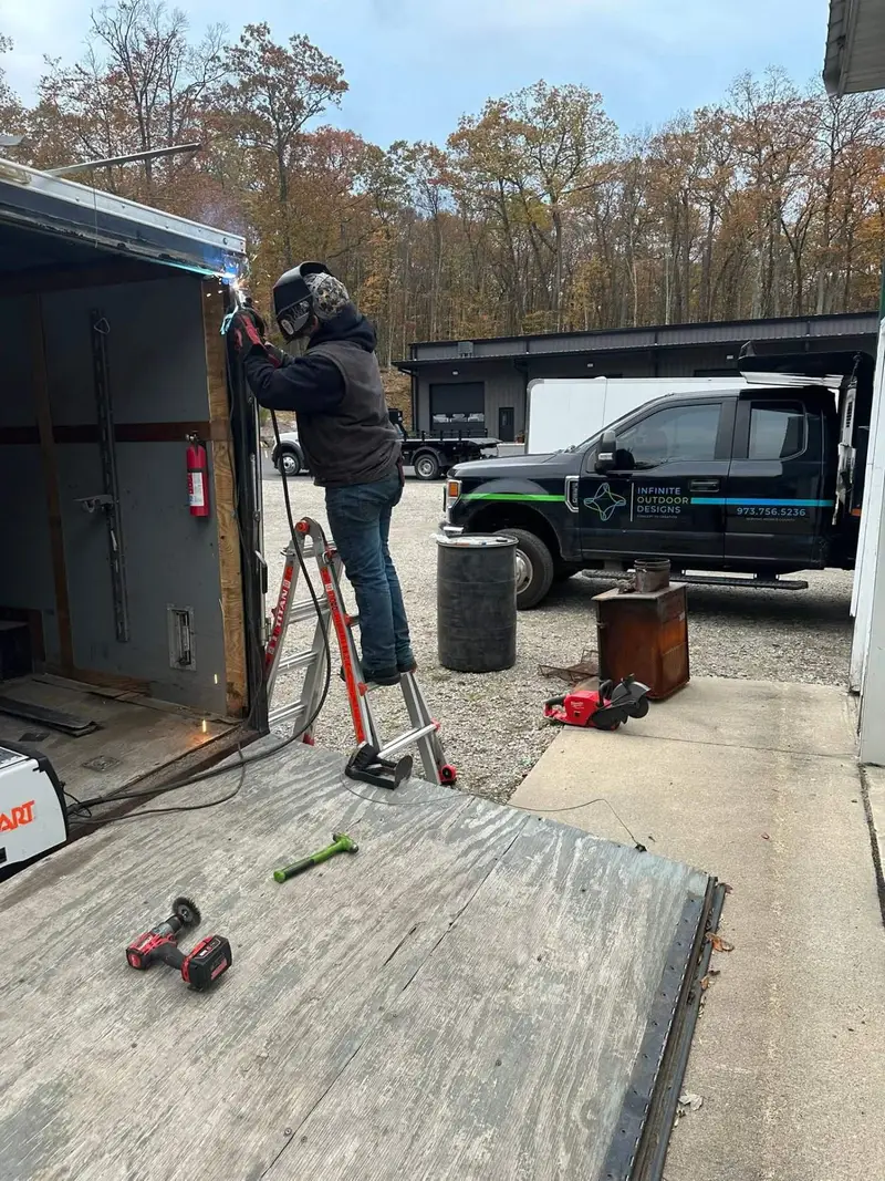 Welder in a helmet repairing the doorway of an enclosed trailer on site