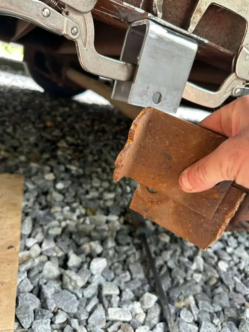 Hand holding a rusted spring hanger removed from under a trailer frame