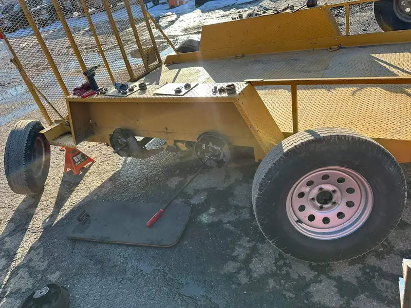 Yellow utility trailer on jack stands with wheels off during an axle and brake rebuild